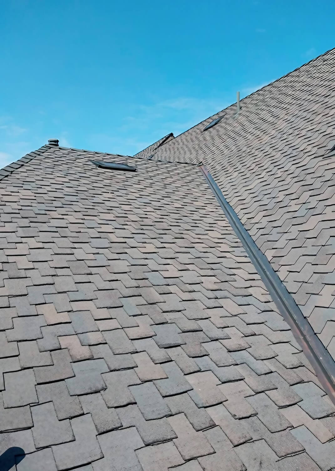 A close-up view of a sloped roof covered with rectangular slate shingles, showcasing a clear blue sky above.