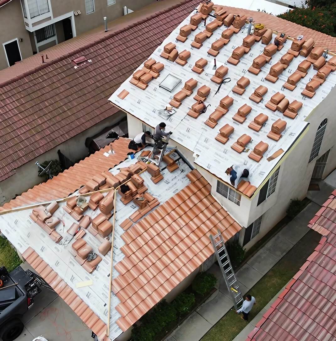Workers installing terracotta roof tiles on a multi-level home, with tools and materials visible on the sloped roofs.